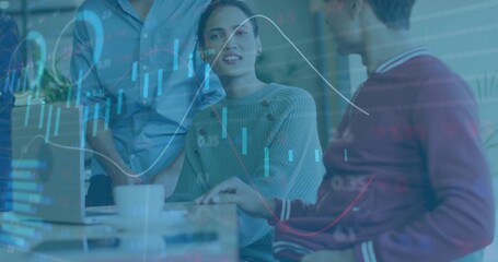 Presenting woman in gray ribbed sweater discussing data at shared workspace, with laptop and charts