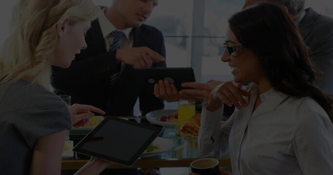 Discussing project, four colleagues in business attire pointing at tablet at office, with breakfast