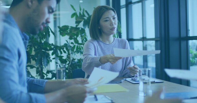 Extending woman in purple sweater handing sheet to colleague at meeting table, with documents - Powered by Adobe