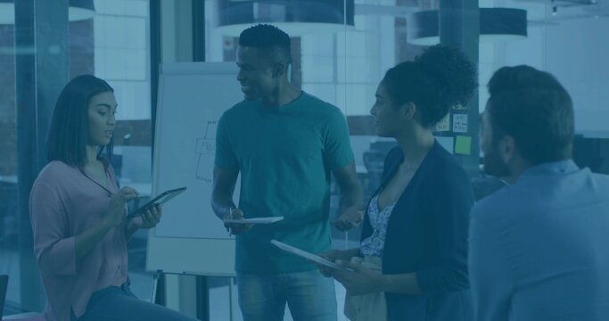 Discussing team of five wearing casual dress in meeting area with flipchart, holding tablet, papers