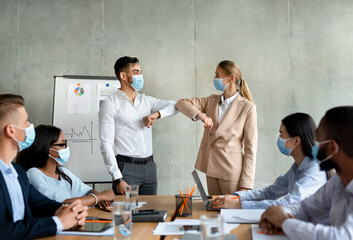 Coworkers greet each other with elbow bumps to maintain social distance during a meeting. Everyone wears masks to protect against COVID-19.