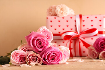 Pink roses with gift box on table against beige background, closeup. Valentine's Day celebration