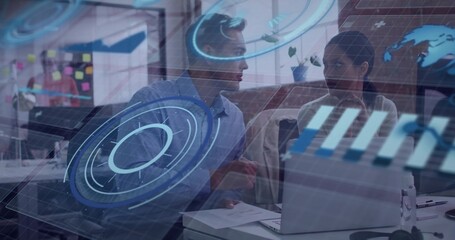 Collaborating two colleagues leaning over laptop in open-plan office, wearing business attire, HUD