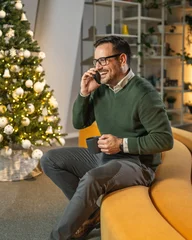 Selbstklebende Fototapeten Sportgeschäft Man making phone call sitting by christmas tree in office  © Miljan Živković