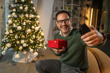 Happy man celebrating christmas holding gift during video call