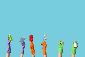 Female hands in rubber gloves with sponges, jar of detergent powder and flower on blue background