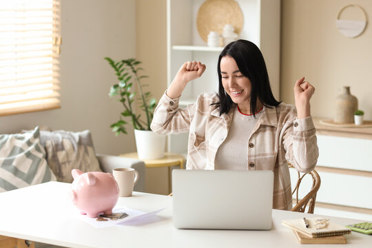 Happy young woman with laptop and money at table in room. Refund concept