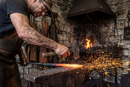Blacksmith striking red hot iron on anvil with hammer in workshop