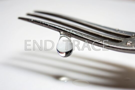 A clear water droplet hanging from a stainless steel fork
