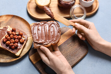 Young woman preparing tasty toast with chocolate spread and hazelnuts on blue grunge background