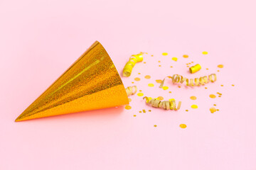 Golden party hat with serpentine and confetti on pink background