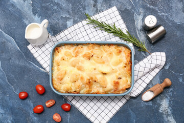 Baking dish with tasty pasta, rosemary, tomatoes and jug of milk on blue grunge background