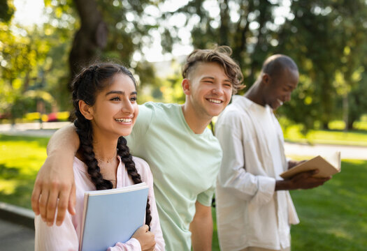 Three friends share a joyful moment in a park under bright sunshine. They enjoy each other's company, with one reading a book while others talk and laugh.