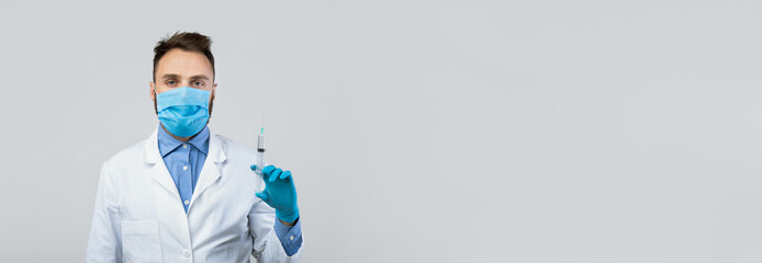 A healthcare worker stands in a clinical space, wearing a mask and gloves, holding a syringe. The worker is focused and ready to assist with vaccinations or medical procedures.