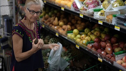 Closeup of smiling attractive mature woman selecting fresh avocados in a grocery store wearing ethnic clothes.
