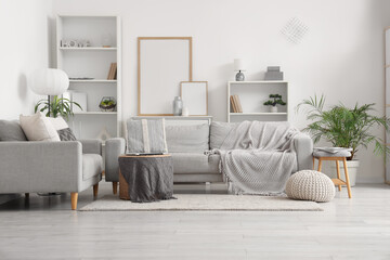 Obraz premium Interior of light living room with grey sofas, soft bench and shelf units