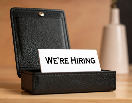 Professional hiring sign in business card holder signifies job opportunity amidst labor market shortages creating serious tone about company recruitment