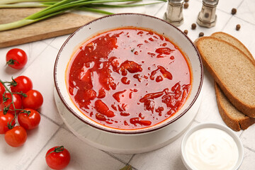 Bowl of tasty Ukrainian borscht and ingredients on white tile background, closeup