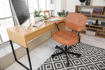 Brown leather swivel chair and workplace with modern computer near window in office