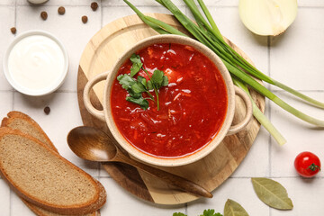 Bowl of tasty Ukrainian borscht and ingredients on white tile background