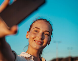 Smiling Young Woman Taking a Sunset Selfie Under Clear Blue Sky