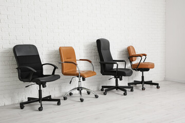 Different office chairs near white brick wall in room