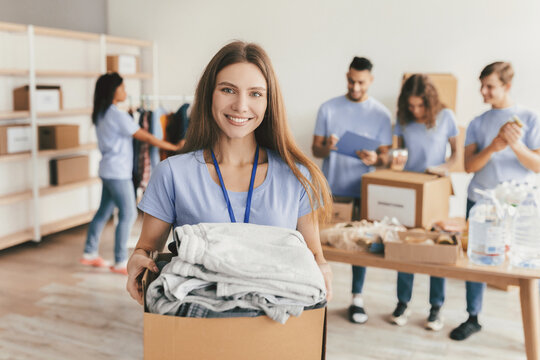 A group of volunteers sorts and distributes donated items at a community center. One volunteer smiles while carrying a box full of clothes, showcasing teamwork and community spirit.