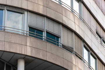 Fototapeta premium Curved facade of a modern office building with large windows, exterior shutters and stone cladding panels