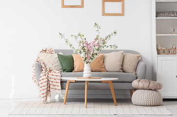 Interior of light living room with flowering branches in vase, table and sofa