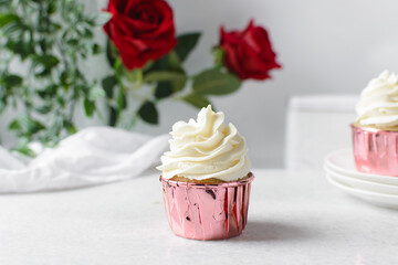 Closeup of a cupcake in pink liners with a vanilla swirl frosting on a white countertop, Pink foil cupcakes with a vanilla buttercream swirl on white background