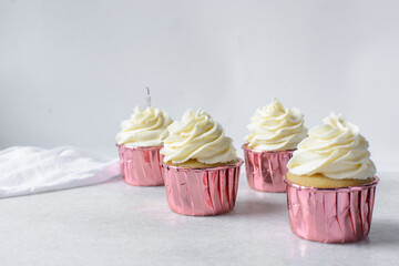 Closeup of a cupcake in pink liners with a vanilla swirl frosting on a white countertop, Pink foil cupcakes with a vanilla buttercream swirl on white background