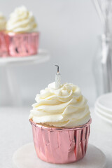 Pink cupcakes with tall buttercream swirl and candle, cupcakes in pink foil liners with vanilla buttercream with candle, frosted cupcakes on a white background