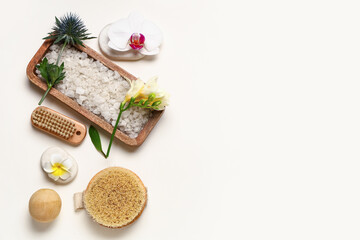 Spa composition with sea salt, massage brushes and flowers on light background