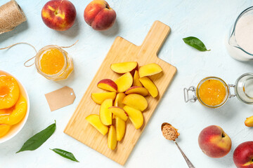 Wooden board with sliced peaches and jars of jam on light blue background