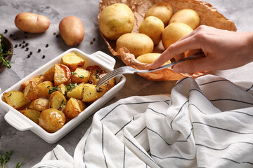 Female hand with fork and baking dish of baked baby potatoes on grey background