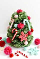 Vibrant green yarn Christmas tree decorated with colorful pom-poms, knitted candy canes, and soft star ornaments, cheerful handcrafted holiday design.