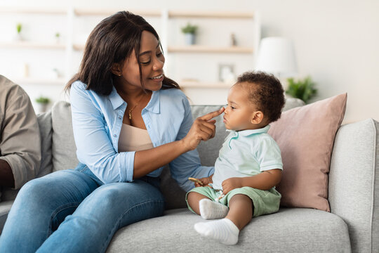 An African American mom smiles as she plays with her cute baby on the couch. They enjoy a happy moment, sharing laughter while bonding in their comfortable living room at home.