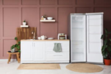 Blurred view of stylish kitchen with empty fridge, counters and shelves