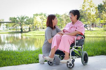 Caring caregiver takes care of elderly patient sitting in wheelchair to breathe fresh air outside. Elderly health care concept. Daughter takes care of sick mother. copy space