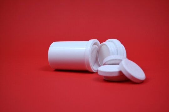 A white pill bottle lies open with several round tablets spilling out onto a red background. Clean, clinical vibe suitable for health, medicine, supplements, and wellness themes.