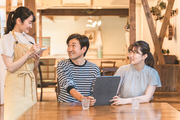 A man and a woman ordering and self-ordering from a menu using a tablet at a cafe, restaurant, or eatery, and a waiter explaining