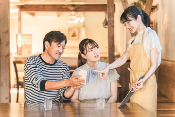 A man and a woman ordering on a smartphone or tablet at a cafe, restaurant, or eatery, and a waiter explaining