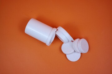 A white pill bottle lies open with several round tablets spilling out onto a orange background. Clean, clinical vibe suitable for health, medicine, supplements, and wellness themes.