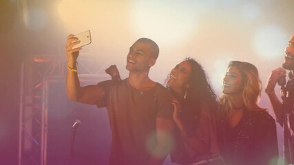 Center man raising smartphone taking selfie, music band leaning, checking drumsticks under lights