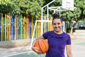 Woman smiling holding basketball on outdoor court