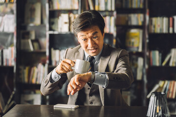 Asian male businessman surprised looking at his watch in the library or study (late, surprised, busy, appointment, schedule)