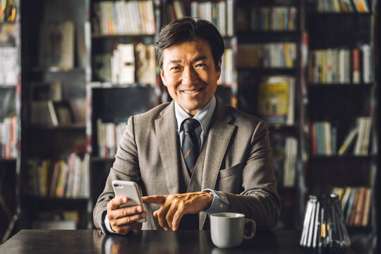 Asian male businessman using smartphone in library, study (e-book, reading, literature, education, app)