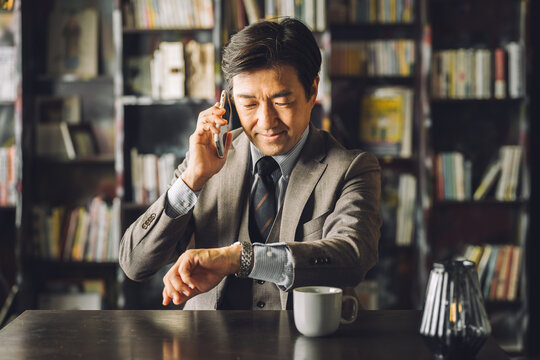 Asian male businessman checking his watch in the library, study (appointment, schedule, time)
