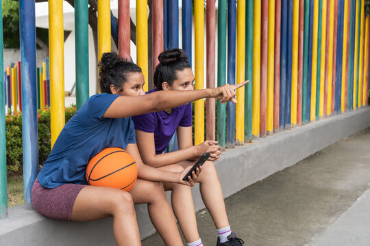 Female basketball players pointing, resting beside colorful fence