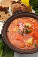 Tasty lentil soup in bowl served on white tiled table, closeup